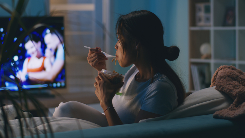 Mulher comendo assistindo tv na sala.