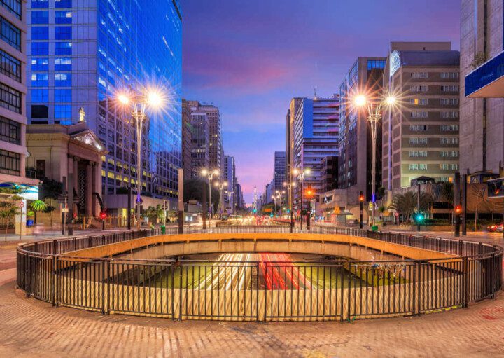 Foto que ilustra matéria sobre o que fazer em SP mostra um viaduto da Avenida Paulista à noite, com prédios altos iluminados em ambos os lados.