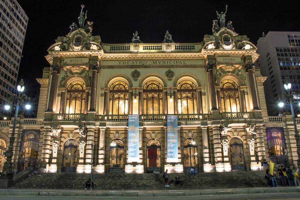 Foto que ilustra matéria sobre o que fazer em SP mostra a fachada frontal do Theatro Municipal de São Paulo toda iluminada à noite. 