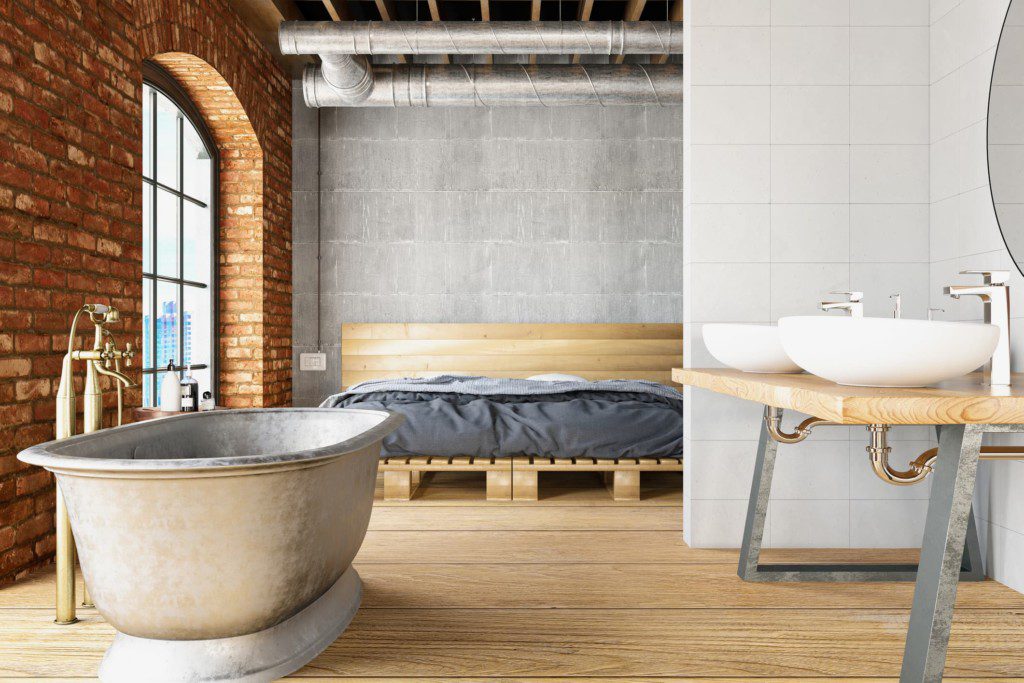Banheiro industrial com revestimento de tijolinhos na parede e madeira no piso. Imagem disponível em Getty Images.