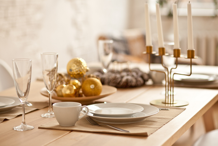 Mesa posta com enfeites de bola dourado, cerâmica branca e castiçal de vela. 