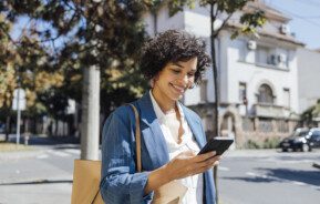 foto que ilustra matéria sobre como usar app quintoandar mostra uma mulher andando na rua mexendo no celular