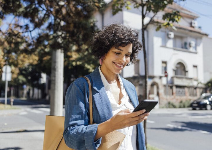 foto que ilustra matéria sobre como usar app quintoandar mostra uma mulher andando na rua mexendo no celular