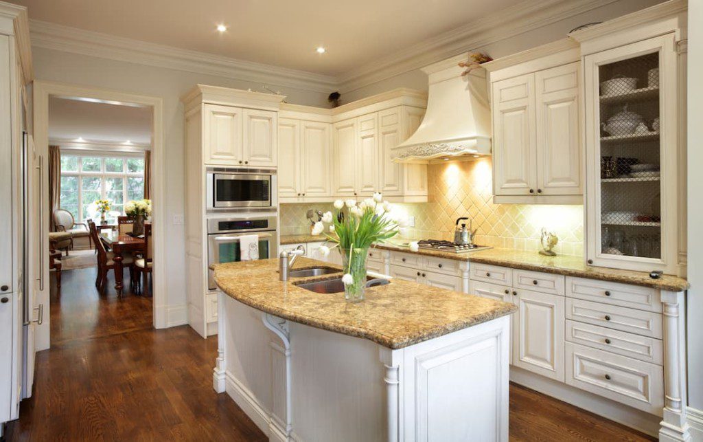 Cozinha clássica com armários brancos e ilha com mármore.