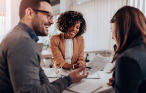 Duas mulheres e um homem conversam sobre um contrato de financiamento imobiliário.