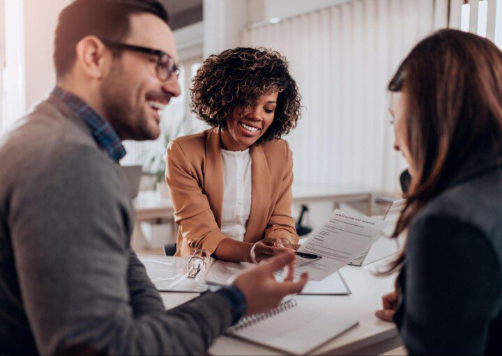 Duas mulheres e um homem conversam sobre um contrato de financiamento imobiliário.