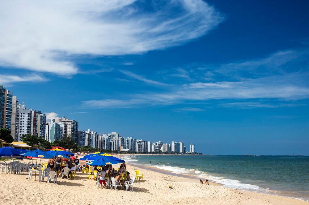 Foto que ilustra matéria sobre bairros de Vila Velha mostra uma visão panorâmica da Praia de Itaparica, com prédios no canto esquerdo, a faixa de areia e o mar no canto direito da imagem.  (Foto: Vitor Jubini | MTur)