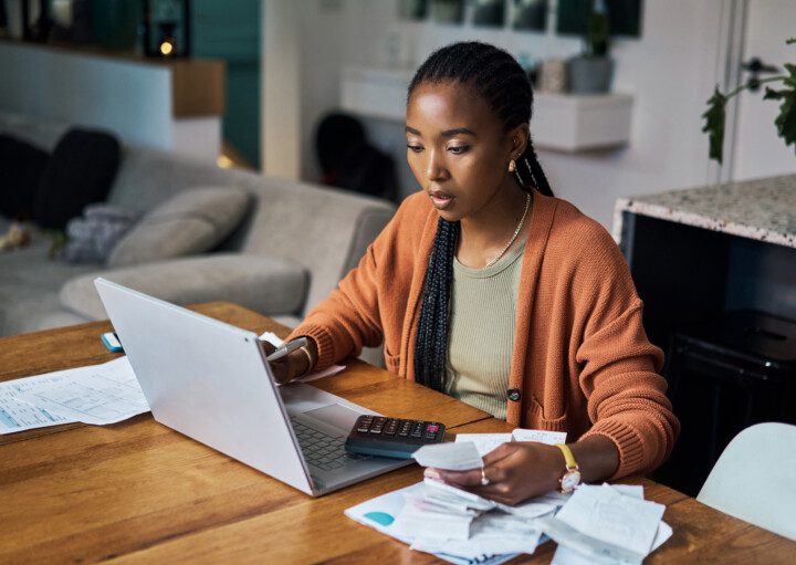 Foto que ilustra matéria sobre INPC mostra uma mulher sentada em uma cadeira com papeís e um notebook aberto sob a mesa.