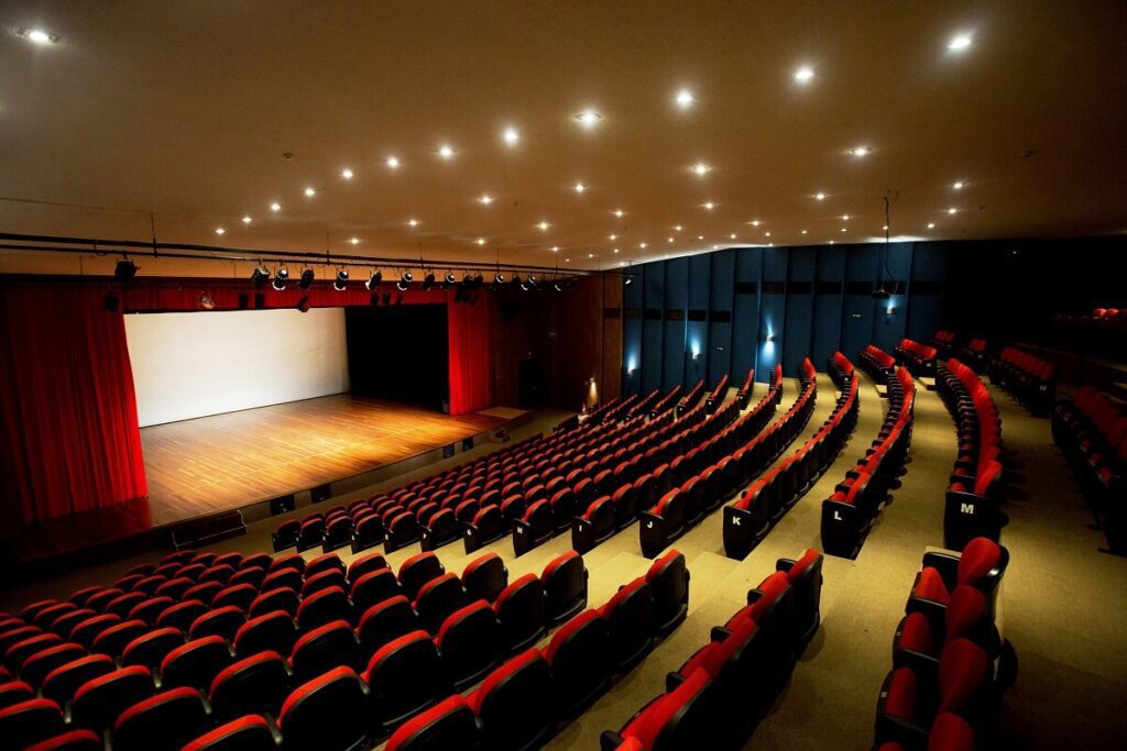 Foto que ilustra matéria sobre o que fazer em Praia Grande mostra o interior do Teatro Serafim Gonzalez, com suas cadeiras vermelhas à direita da imagem e o palco à esquerda.