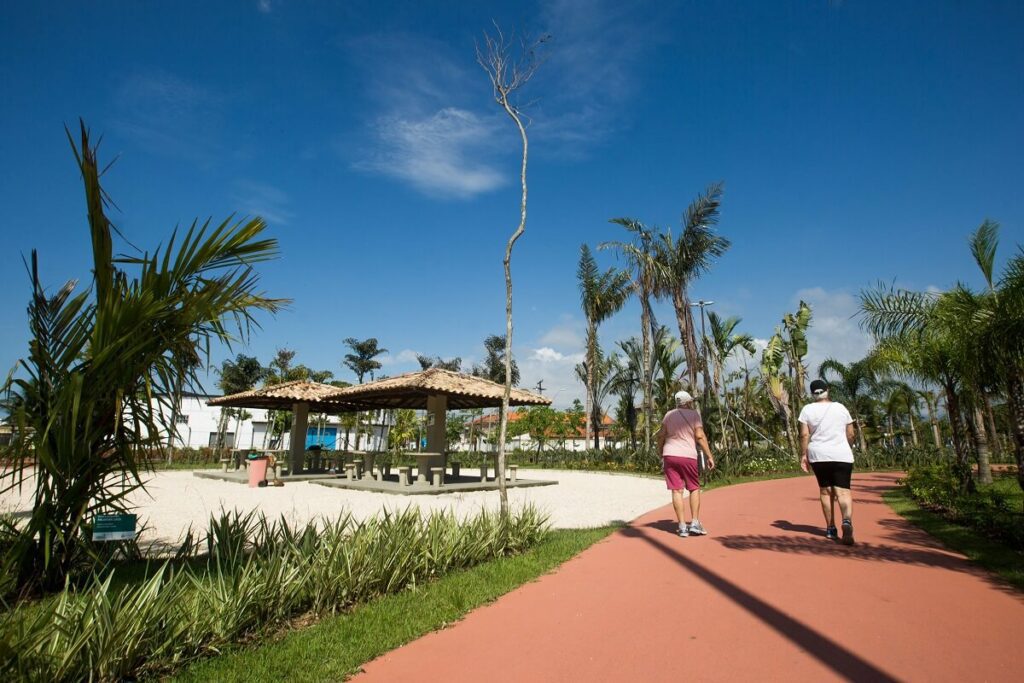 Foto que ilustra matéria sobre o que fazer em Praia Grande mostra pessoas andando uma pista de caminhada em meio a jardins no Parque da Cidade.
