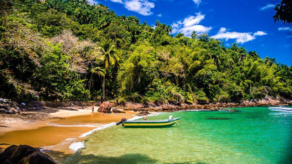 Imagem com vista para a Ilha das Couves, em Ubatuba. Com mar, vegetação e barco. 