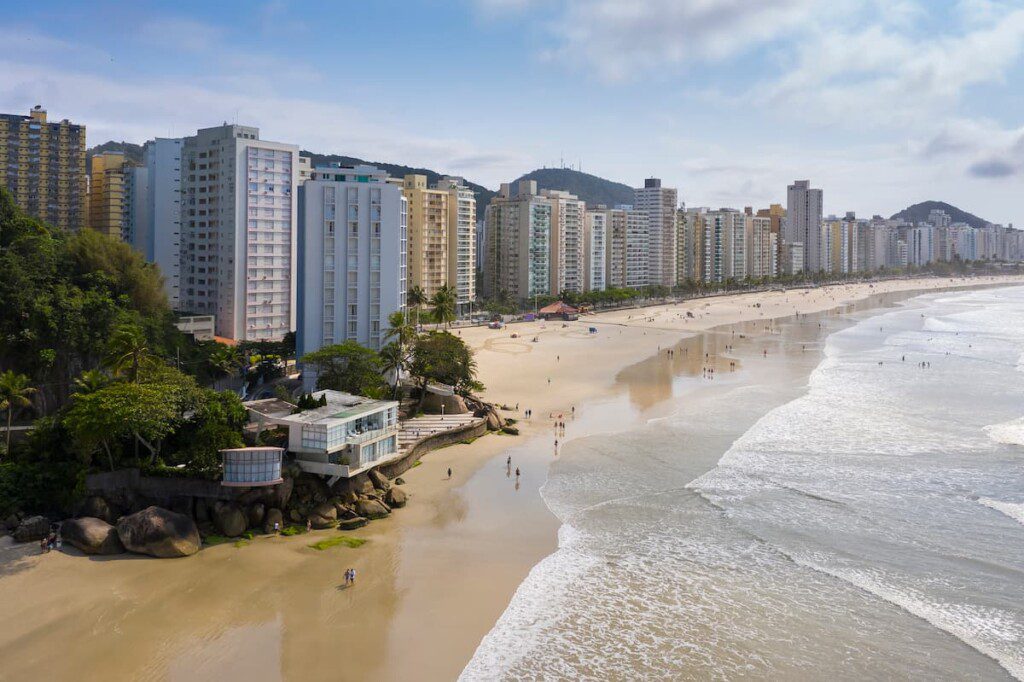 Imagem aérea da Praia das Astúrias. Na foto é possível ver o litoral e os prédios que contornam a praia.