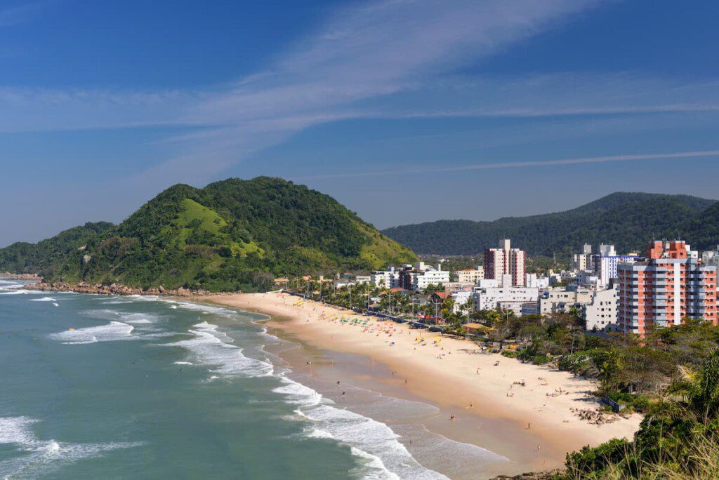 Fotografia aérea da orla da Praia do Tombo. É possível ver prédios que cercam a faixa de areia e um pouco de Mata Atlântica.