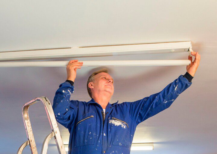 Foto que ilustra matéria sobre zelador mostra um homem com um macacão azul trocando uma lâmpada