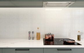 Imagem de um backsplash revestido de azulejo branco por trás de um balcão branco com cooktop, panelas e temperos