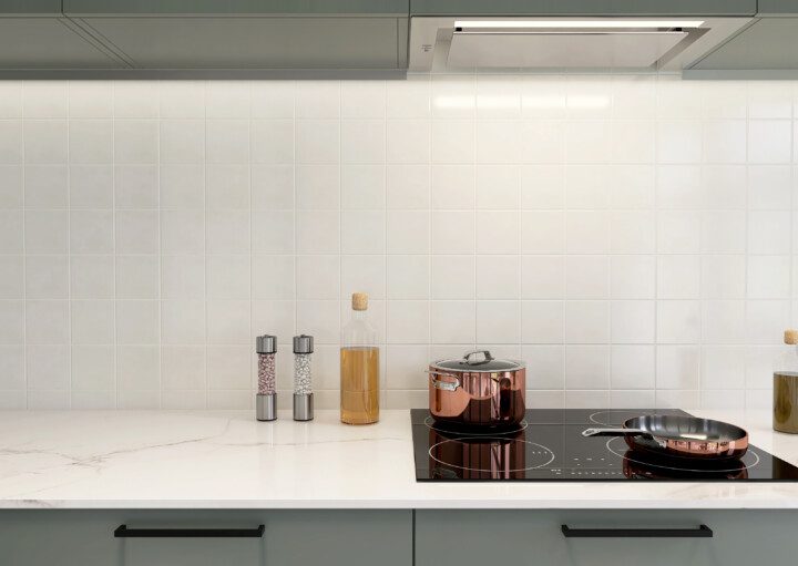 Imagem de um backsplash revestido de azulejo branco por trás de um balcão branco com cooktop, panelas e temperos