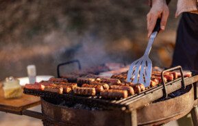 Imagem de uma pessoa fazendo churrasco em uma grela acesa enquanto segura uma espátula