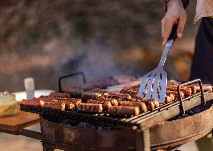 Imagem de uma pessoa fazendo churrasco em uma grela acesa enquanto segura uma espátula