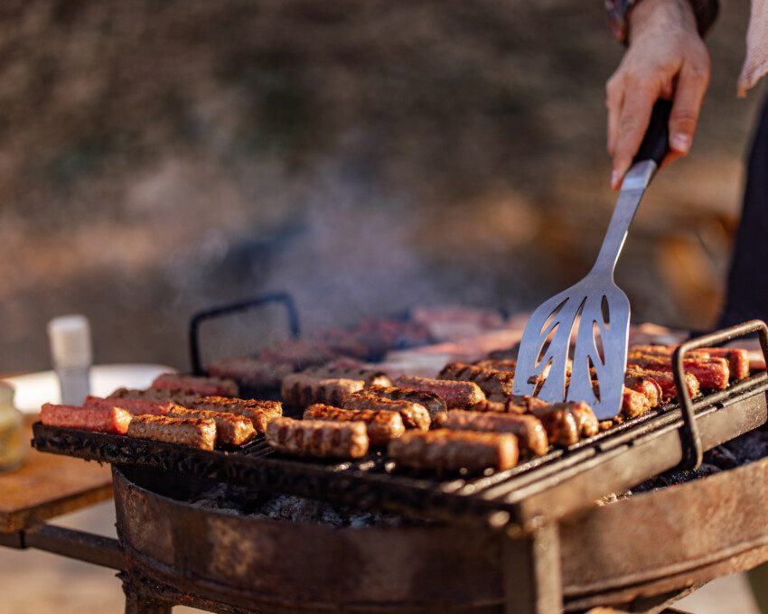 Imagem de uma pessoa fazendo churrasco em uma grela acesa enquanto segura uma espátula