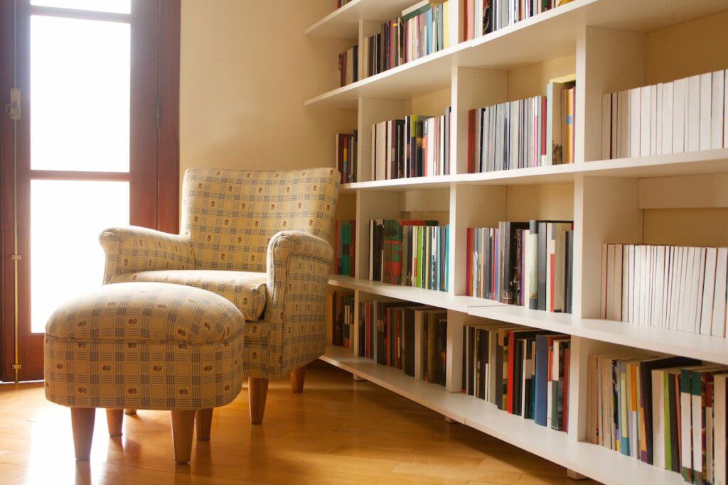 Cantinho de leitura no quarto, com poltrona bege e estante para livros.