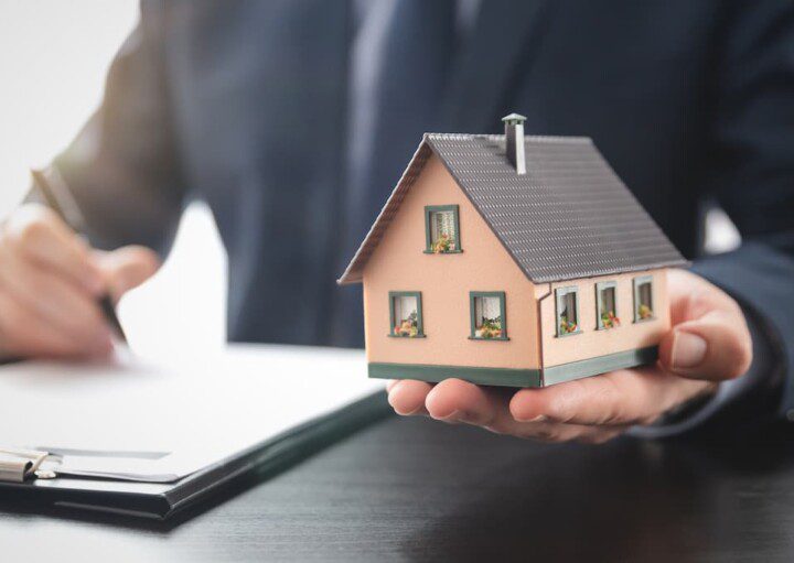 Representante de incorporadora assina um contrato e entrega a miniatura de uma casa.