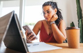 Foto que ilustra matéria sobre reforma tributária 2023 mostra mulher vendo o celular e o tablet que estão sob a mesa