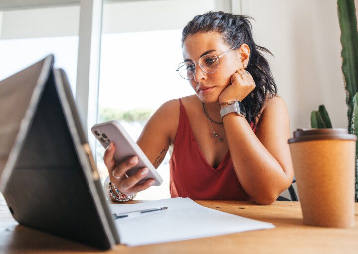 Foto que ilustra matéria sobre reforma tributária 2023 mostra mulher vendo o celular e o tablet que estão sob a mesa