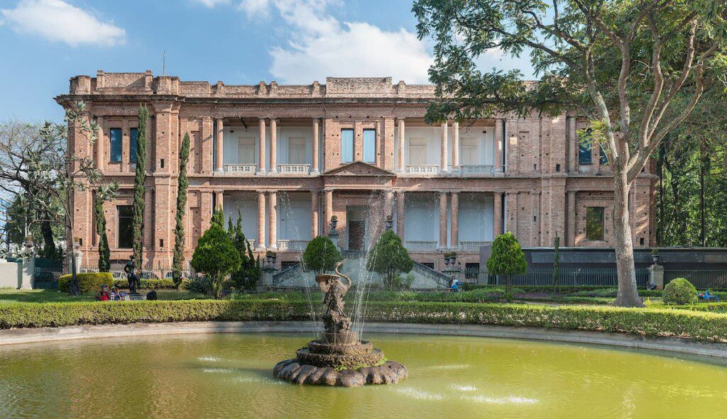 Prédio histórico da Pinacoteca de São Paulo, com uma fonte e jardim em frente a sua fachada.