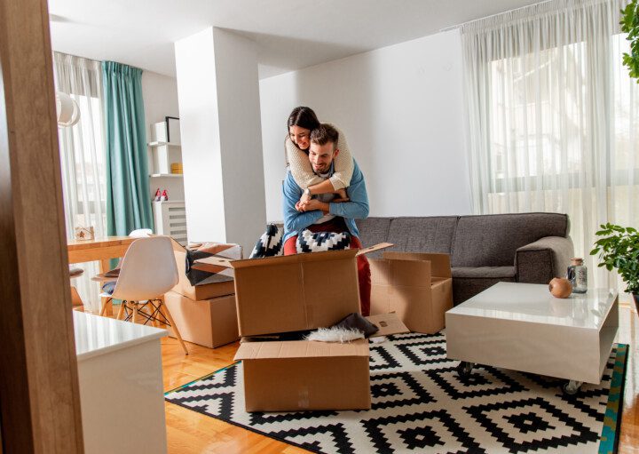 Imagem de um casal composto por uma mulher e um homem abrindo uma caixa em um apartamento mobiliado para ilustrar matéria sobre as vantagens de morar em apartamento