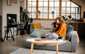 Imagem de uma mulher sentada no sofá da sala com o telefone no ouvido para ilustrar matéria sobre apartamento funcional