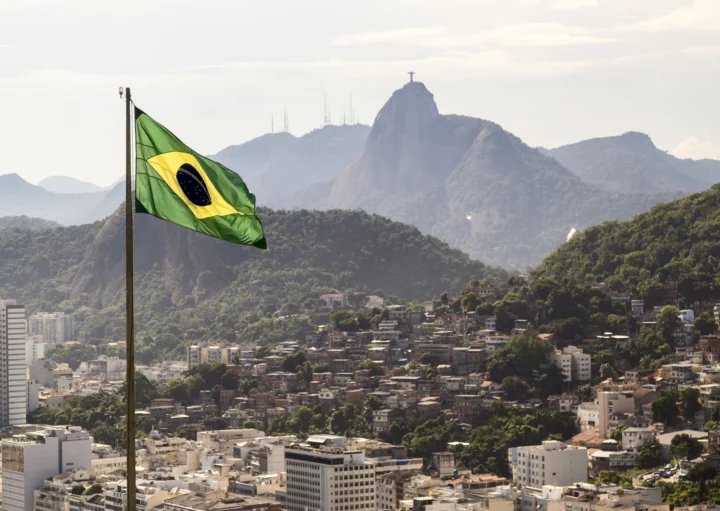 Imagem de uma bandeira brasileira na frente do Corcovado e vários prédios da região para ilustrar matéria sobre o IDH dos estados brasileiros