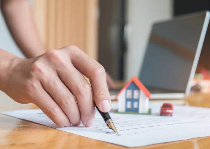 Imagem de uma pessoa assinando um contrato em cima de uma mesa com a figura de uma casa de miniatura ao fundo para ilustrar matéria sobre assinei o contrato de financiamento, posso desistir?