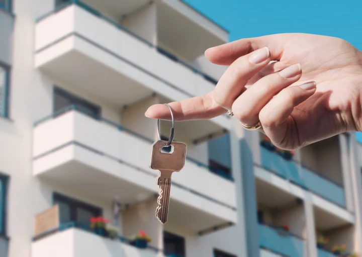 Imagem de uma mão feminina segurando a chave de um imóvel em frente a um prédio residencial para ilustrar matéria sobre como escolher um bom apartamento