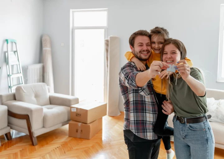 Imagem de um casal composto por um homem e uma mulher, ao lado de uma criança, segurando a chave da nova casa para ilustrar matéria sobre melhor época para alugar apartamento