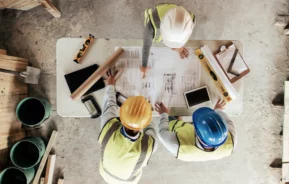 Vista superior de homens em um canteiro de obras olhando para o projeto em cima de uma mesa para ilustrar matéria sobre taxa de ocupação