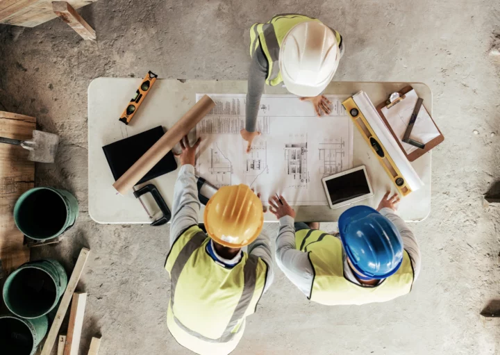 Vista superior de homens em um canteiro de obras olhando para o projeto em cima de uma mesa para ilustrar matéria sobre taxa de ocupação