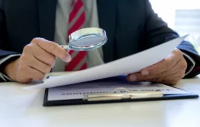 Fotografia de um homem de paletó analisando um documento para não cair em golpes imobiliários.