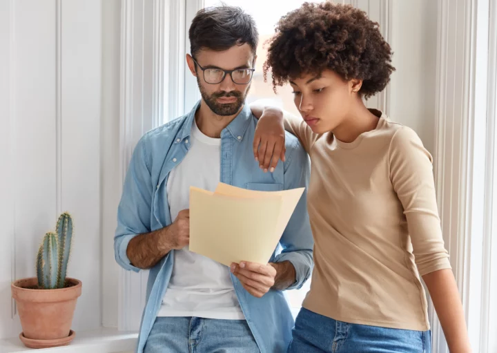 Imagem de um casal composto por um homem e uma mulher um ao lado do outro concentrados em ler as informações descritas em um papel para ilustrar matéria sobre multa por quebra de contrato por parte do locador