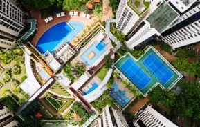 Imagem aérea de um condomínio residencial com piscinas e quadras esportivas para ilustrar matéria sobre o que é incluso no condomínio de um apartamento