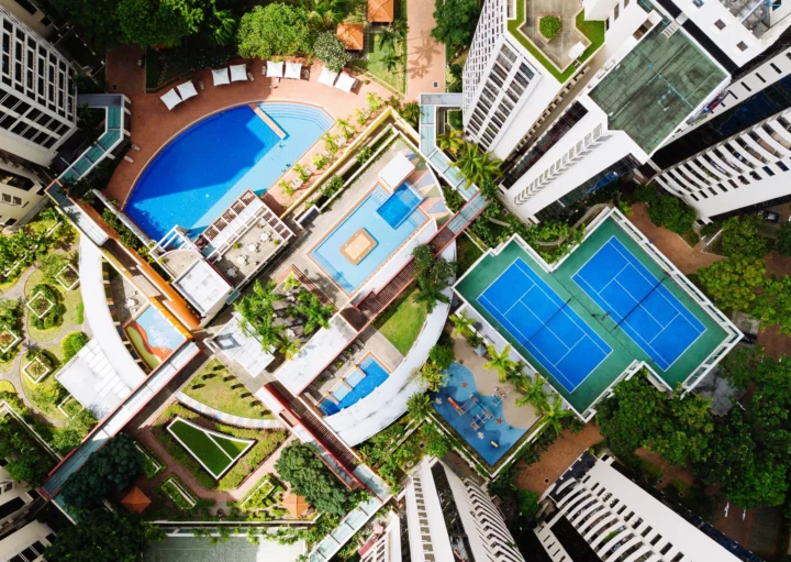 Imagem aérea de um condomínio residencial com piscinas e quadras esportivas para ilustrar matéria sobre o que é incluso no condomínio de um apartamento