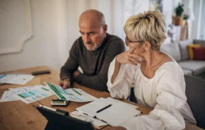 imagem que ilustra matéria sobre IOF financiamento imobiliario mostra um casal sentado em frente à uma mesa cheia de papeis