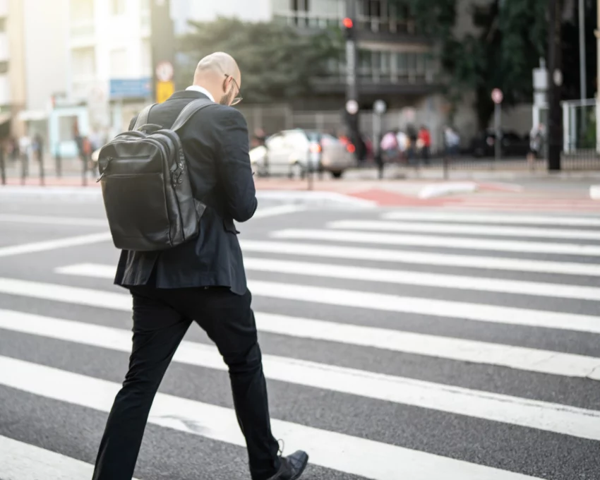 Imagem de um homem de costas vestindo terno preto com uma mochila nos ombros cruzando uma faixa de pedestres na Avenida Paulista para ilustrar matéria sobre o centro expandido de São Paulo