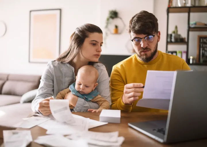 Um homem, sua espeso e filho estão na frente de um computador analisando documentos.