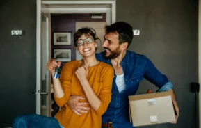 Imagem de um homem e uma mulher felizes segurando a chave da casa nova para ilustrar matéria sobre prédio antigo