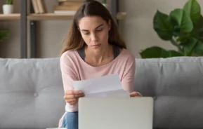 Foto que ilustra matéria sobre cota condominial mostra uma jovem mulher segurando e olhando para um papel com um semblante preocupado (Foto: Shutterstock)