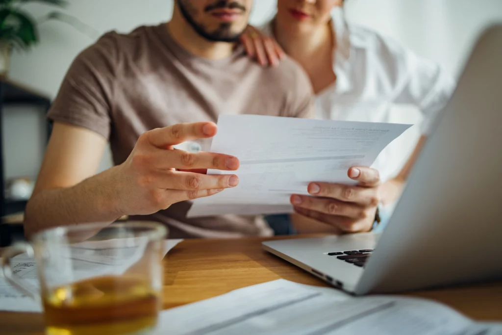 Imagem de um casal em uma mesa olhando a tela do computador e alguns papéis com semblante sério para ilustrar matéria sobre as coberturas do seguro fiança