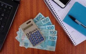 Foto que ilustra matéria com números na tabela IGP-M mostra uma calculadora em cima de algumas notas de 100 reais e ao lado de um calendário, um bloquinho, uma caneta, um celular e um notebook (Foto: Shutterstock)