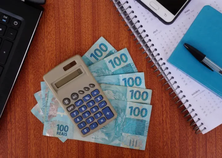 Foto que ilustra matéria com números na tabela IGP-M mostra uma calculadora em cima de algumas notas de 100 reais e ao lado de um calendário, um bloquinho, uma caneta, um celular e um notebook (Foto: Shutterstock)