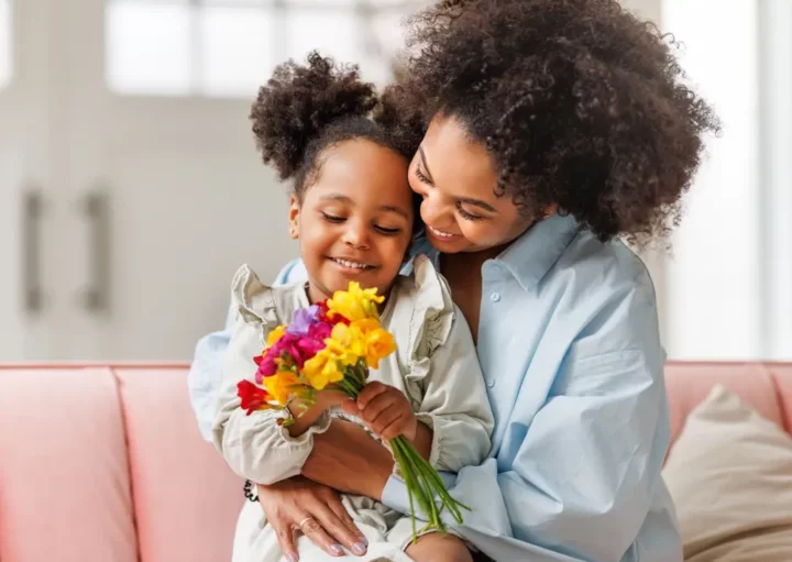 Foto que ilustra matéria sobre decoração para dia das mães mostra uma menina sentada no colo de sua mãe enquantro segura um buquê de flores (Foto: Shutterstock)