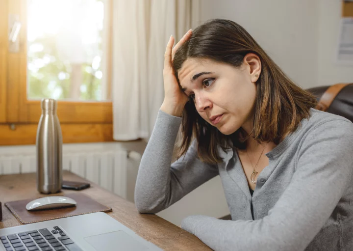 Imagem que ilustra matéria sobre se é possível alugar imóvel com nome sujo mostra mulher sentada em frente ao computador com uma cara de preoucupada